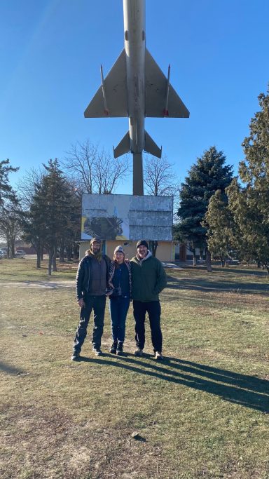 Three people stand in front of a large missile sign in an outdoor setting.